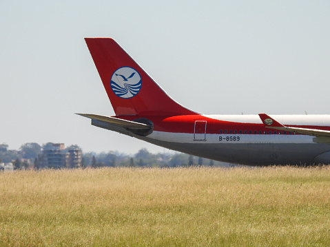 A Sichuan Airlines Airbus A330-343 plane, registration B-8589, has landed at Sydney Kingsford-Smith Airport as flight 3U3883 from Chengdu and is taxiing to the international terminal. In the distance are residential buildings. This image was taken from Mill Stream Lookout, Botany Bay on a hot and sunny afternoon on 25 February 2024.