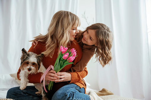 Holding flowers for mother's day holiday, embracing, with dog. Parent with daughter at home.