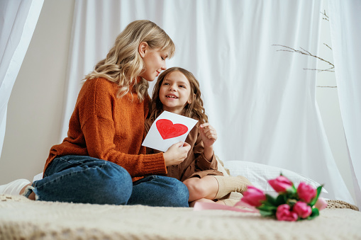 Red paper heart shaped present for mother's day. Female parent with daughter is at home.