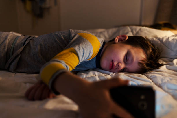 istock A carefree boy is lying in bed at home, holding a smartphone in his hand while sleeping. 2047778483