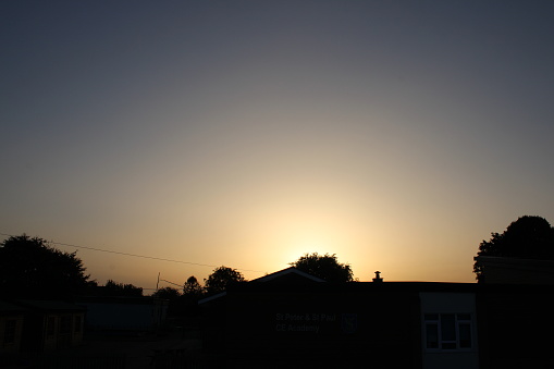 Sun setting in sky, silhouette of trees and rooftops in background