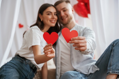 Holding paper hearts. Young couple are together at home.