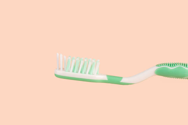istock Green and white plastic toothbrush with comfortable handle isolated on an apricot colored background. 2047789403