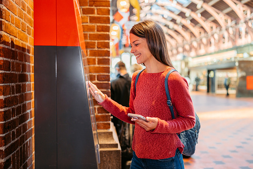Young woman buying train tickets using smartphone at the train station in Copenhagen in Denmark.