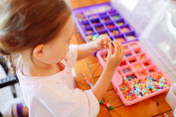 Close-up of a child's hands threading colorful beads onto a string, concentrating on creating a handmade bracelet. This image captures creativity, fine motor skills, and playful learning.
