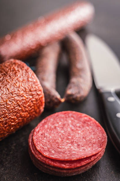 Sliced smoked salami sausages on the black table.