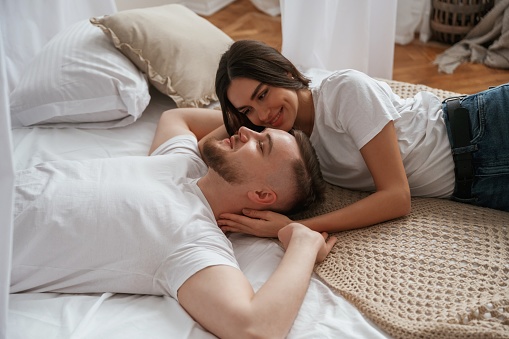 On the bed, lying down and smiling. Young couple are together at home.