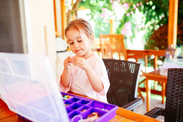 Mother with her daughter making beaded jewelry at home, closeup