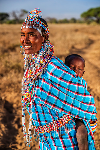 African mother from Masai tribe carrying her baby , Kenya, Africa. Mount Kilimanjaro on the background, central Kenya, Africa. Maasai tribe inhabiting southern Kenya and northern Tanzania, and they are related to the Samburu.