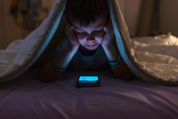 istock Boy playing games on mobile phone while lying on bed in bedroom under the blanket. He is hiding there. 2047825333