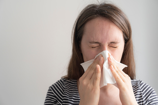 young woman feeling ill and blowing her nose with a tissue