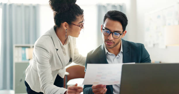 istock Documents, discussion and business people with laptop, advice and collaboration for agenda, schedule or sales. Creative agency, businessman and woman at desk with report, paperwork and feedback chart 2047840717