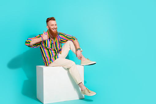 Full body size photo of cheerful red hair businessman showing thumb up like symbol when sitting on podium over cyan color background.