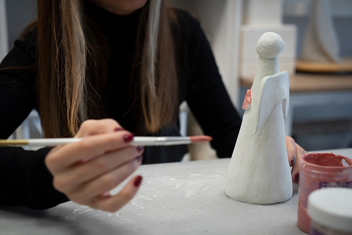 Skillful young woman in apron painting art product at workshop