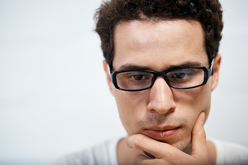 Face of curly-haired young man in horn-rimmed glasses looking thoughtful.