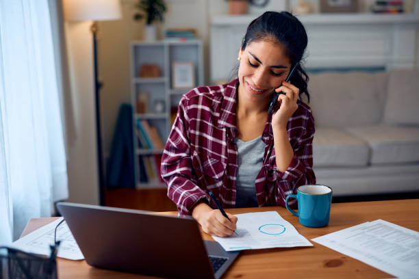 istock Happy Latin American woman talking on mobile phone while working at home. 2047876004