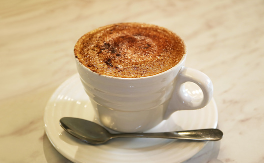 Cup of mouthwatering frothy cappuccino coffee on white table