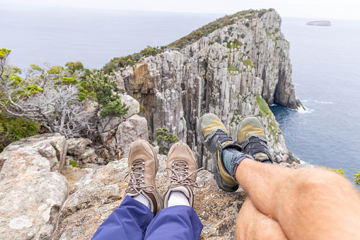 Personal perspective of their feet hanging by a cliff of a peninsula in Tasmania, seascape view.
