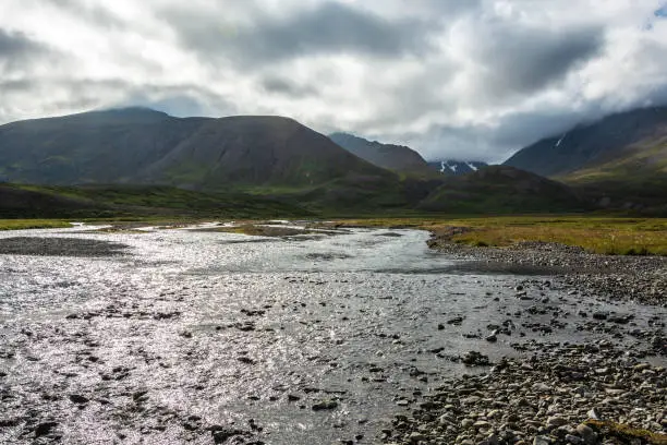 Photo of Icelandic landscape with river and mountains under cloudy sky in summer