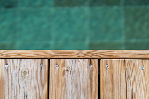 Poolside wooden deck and turquoise blue water of pool, view from the top