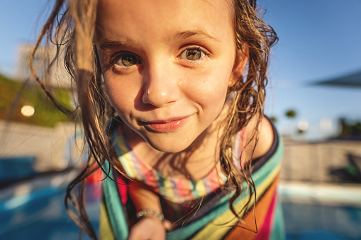 summer portrait of a little girl with wet hair in a towel, after a swim in the pool