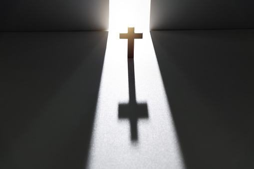 A wood cross on an old church steeple backlighted by a rising sun. Some copy space.