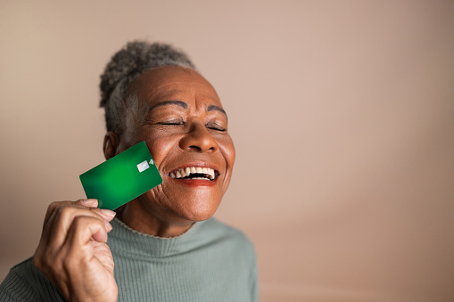 Senior woman with eyes closed holding a credit card on a beige background