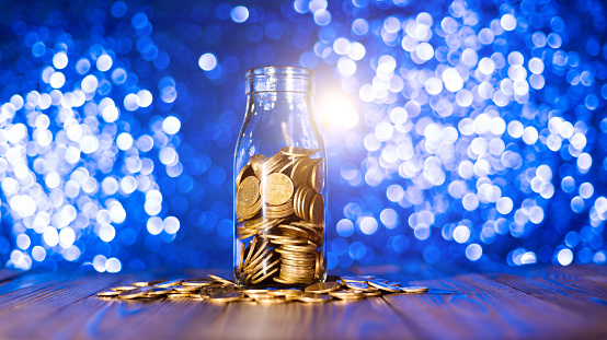 Glass jar with coins on shiny background