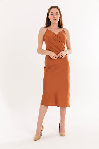 Brunette young woman wearing short-sleeved, orange color dress.  Strapless sleeveless dress wool dress, brown high heels shoes.