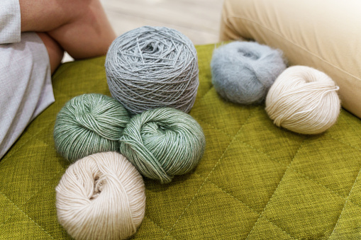 Balls of wool in pastel colors lying on the green sofa at the yarn store. Knit craft studio
