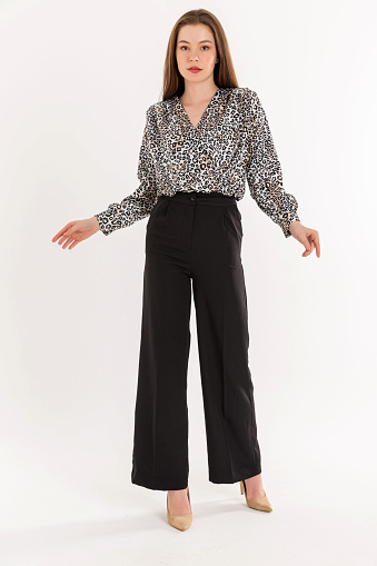 Brunette young woman wearing long-sleeved blouse and loose pants.   brown high heels shoes.