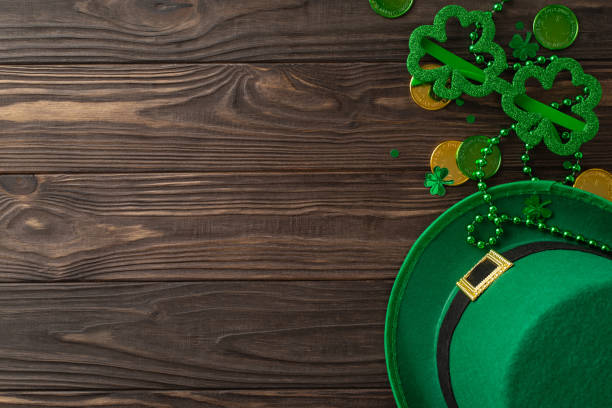 istock Enthralling St. Patrick's layout seen from top view, incorporating clovers, magic hat, coinage, humorous glasses, strings, confetti, neatly organized on timber background, empty spot for text or ads 2047995768
