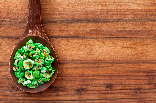 Top view of wooden spoon over table with green dyed popcorn on it