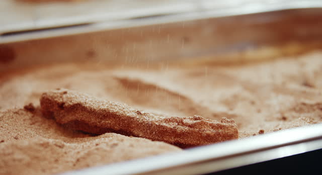 coating churro with sugar + cinnamon with metal tongs in festival booth