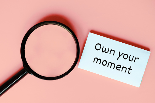 Own your moment on white notepad on pink background.