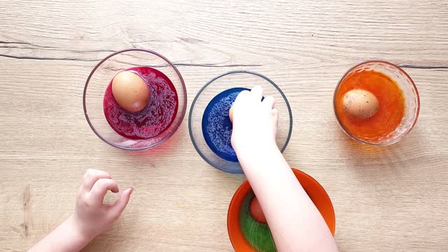 Hands of a girl child coloring festive Easter eggs with colorful dyes on the table at home