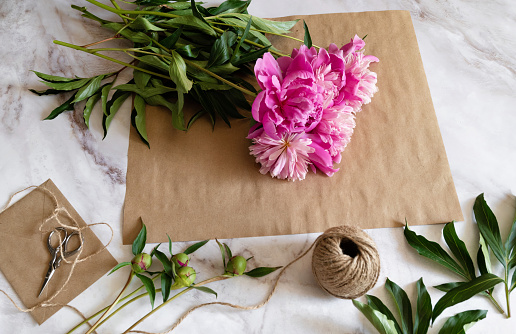 A female florist makes a bouquet of peony flowers wrapped in kraft paper on her desktop. View from above. High quality photos