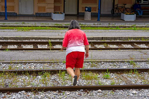 Middle aged woman crossing railway tracks at train station of Slovenian City of Kranj on a cloudy summer day. Photo taken August 9th, 2023, Kranj, Slovenia.
