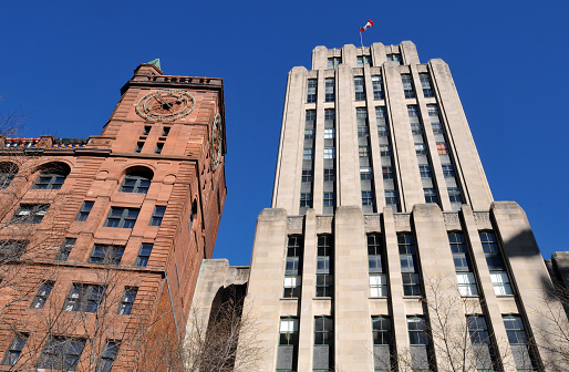 Montreal, QC, Canada, Nov. 8, 2023: The historic sandstone New York Life Insurance Building, also known as the Quebec Bank Building (left) stands beside the Art Deco Aldred Building in Old Montreal's Place d'Armes.