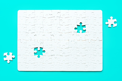 Blank white rectangular puzzle with two final pieces set aside on a serene blue background. Challenge and creativity related concept.