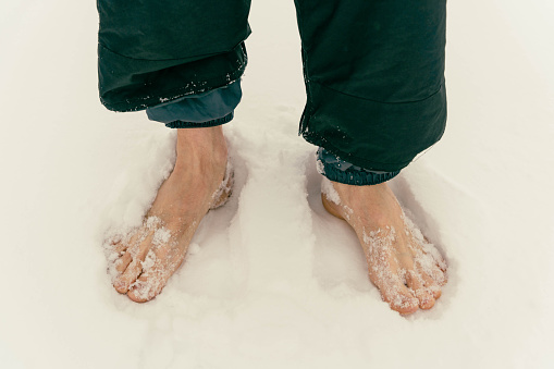 Men's bare feet are standing on the snow. Cold hardening concept