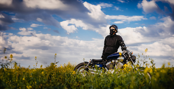 male motorcyclist on a retro custom motorcycle in a blooming yellow field in summer.