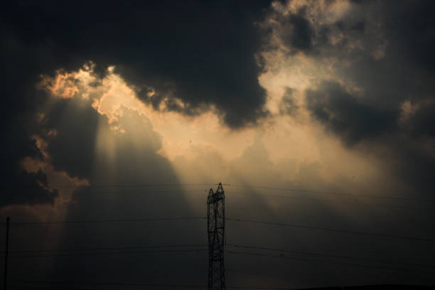 Thick clouds on an overcast day split the sunlight into bundles and shrouded the power line towers