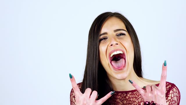 Young Woman Posing With Devil Horns Gesture And Sticking Out Tongue Isolated On A White Background
