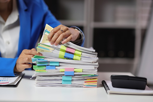 Businesswoman hands working in Stacks of paper files for searching and checking unfinished document achieves on folders papers at busy work desk office.