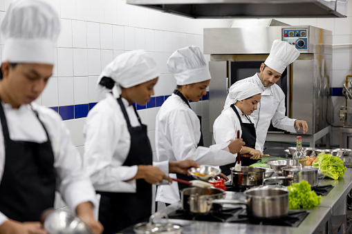 Latin American chef teaching a class to a group of students in cooking school - education concepts
