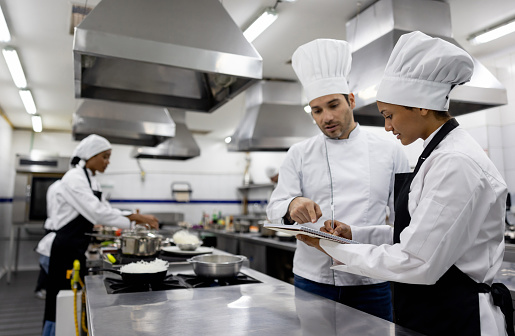 Chef talking to a student in a cooking class while she writes it down a recipe on a notebook