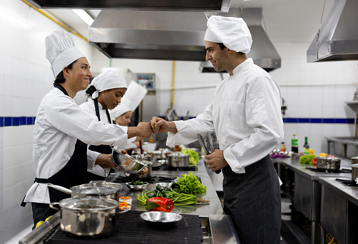 Happy chef congratulating a student in a cooking class giving him a fist bump