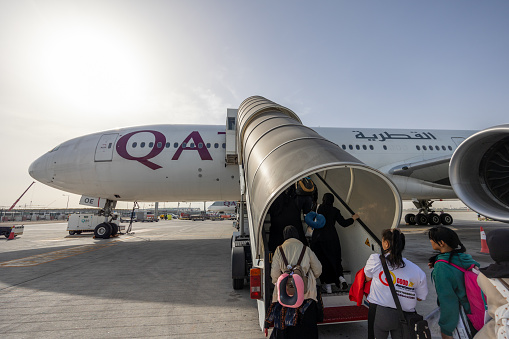 Doha, Qatar - February 20, 2024 : Passengers board a Boeing 777-300ER aircraft, operated by Qatar Airways at the Hamad International Airport in Doha, Qatar.