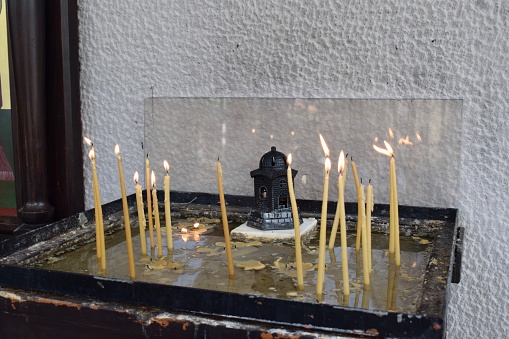 Burning candles in a small memorial outside of a Greek Orthodox Church in Skiathos town (Cathedral of the Three Hierarchs). Thin candles in a sandbox, Greece.